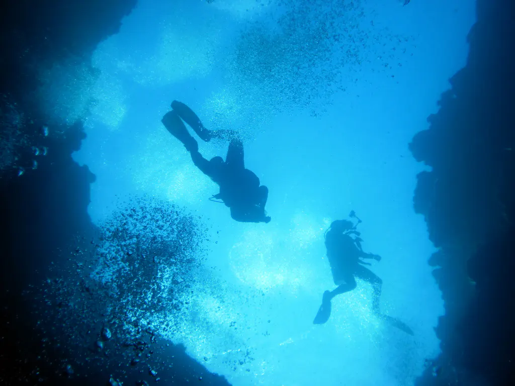 Looking up as two divers prepare to enter the cavern through one of the blue holes.   At the depth at which this photo was taken, the water's surface is no longer clearly visible.