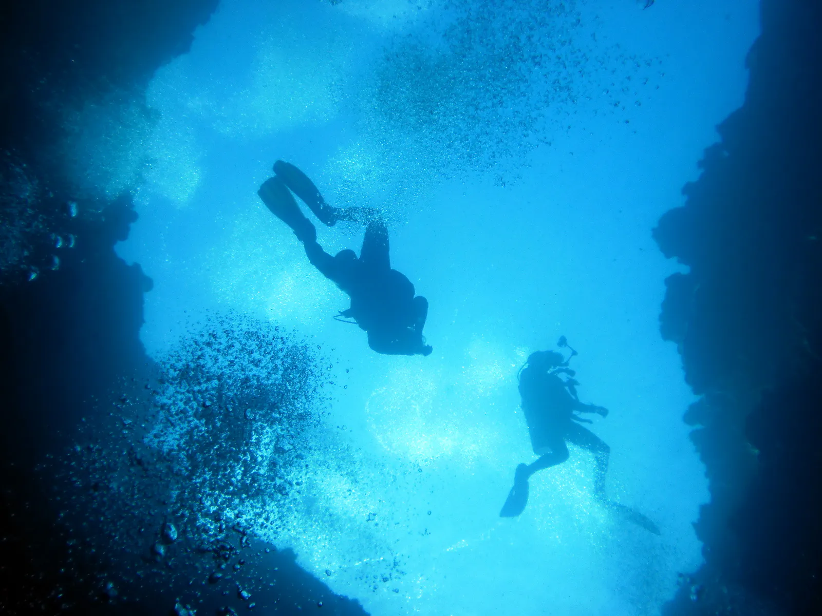 Looking up as two divers prepare to enter the cavern through one of the blue holes. At the depth at which this photo was taken, the water's surface is no longer clearly visible.