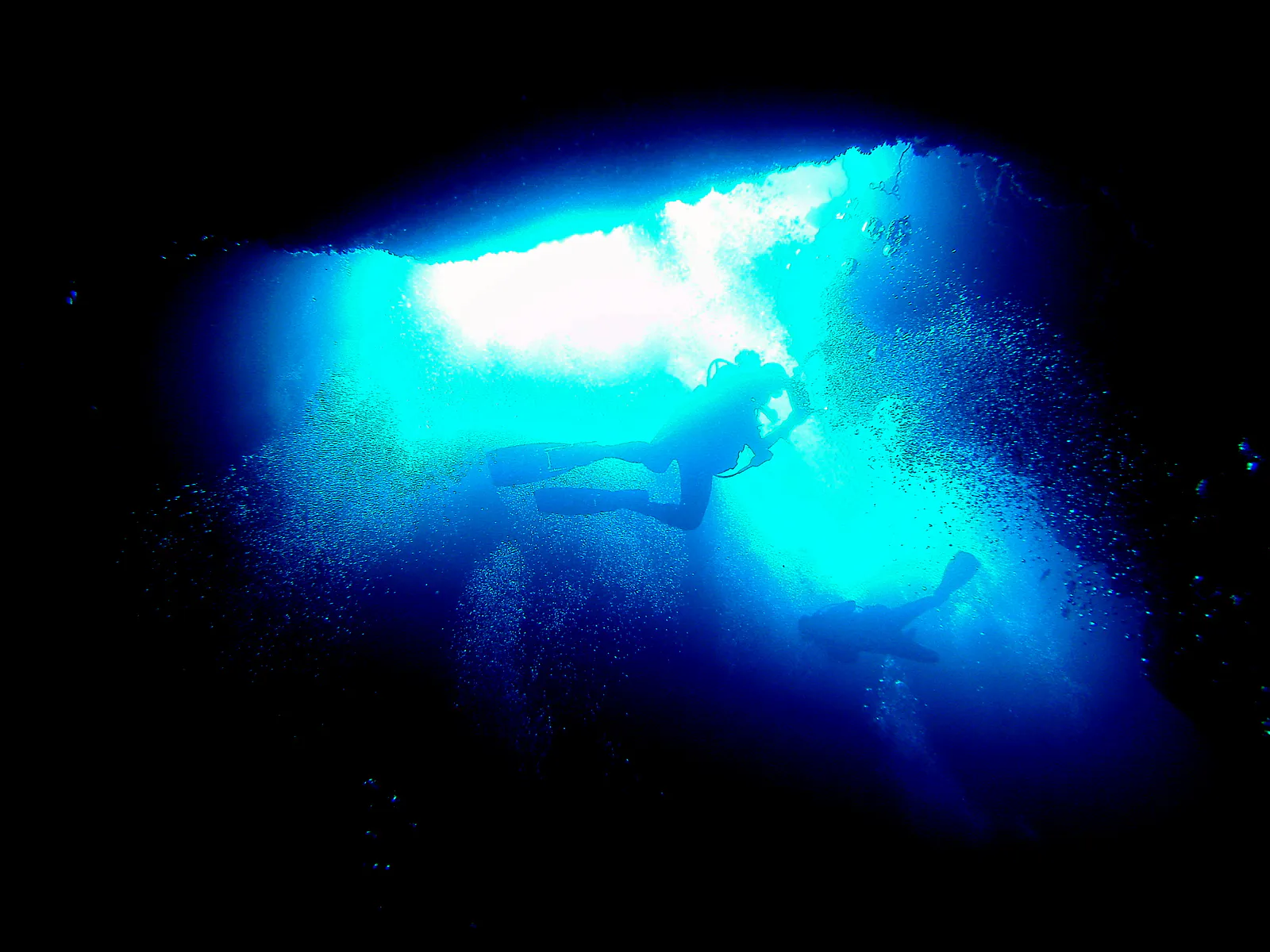 Looking from the cavern up toward two divers swimming in the light of one of the blue holes above.
