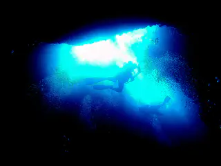 Looking from the cavern up toward two divers swimming in the light of one of the blue holes above.