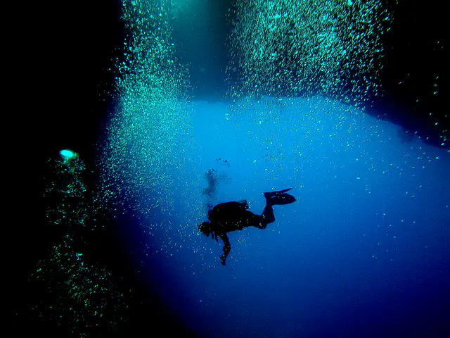 A diver whose silhouette is back-lighted by one of the caverns two exits along the reef wall.