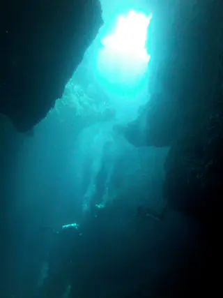 Three divers descend into the cavern from one of the Blue Holes at the reef top.