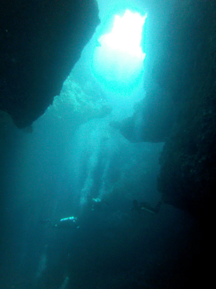Three divers descend into the cavern from one of the Blue Holes at the reef top.