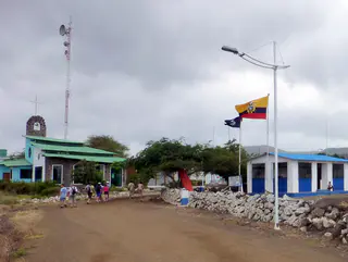 Floreana - Puerto Velasco Ibarra Harbor.  Church on let and Ecuadorian Naval Post on right.  Group is walking to the Chiba.